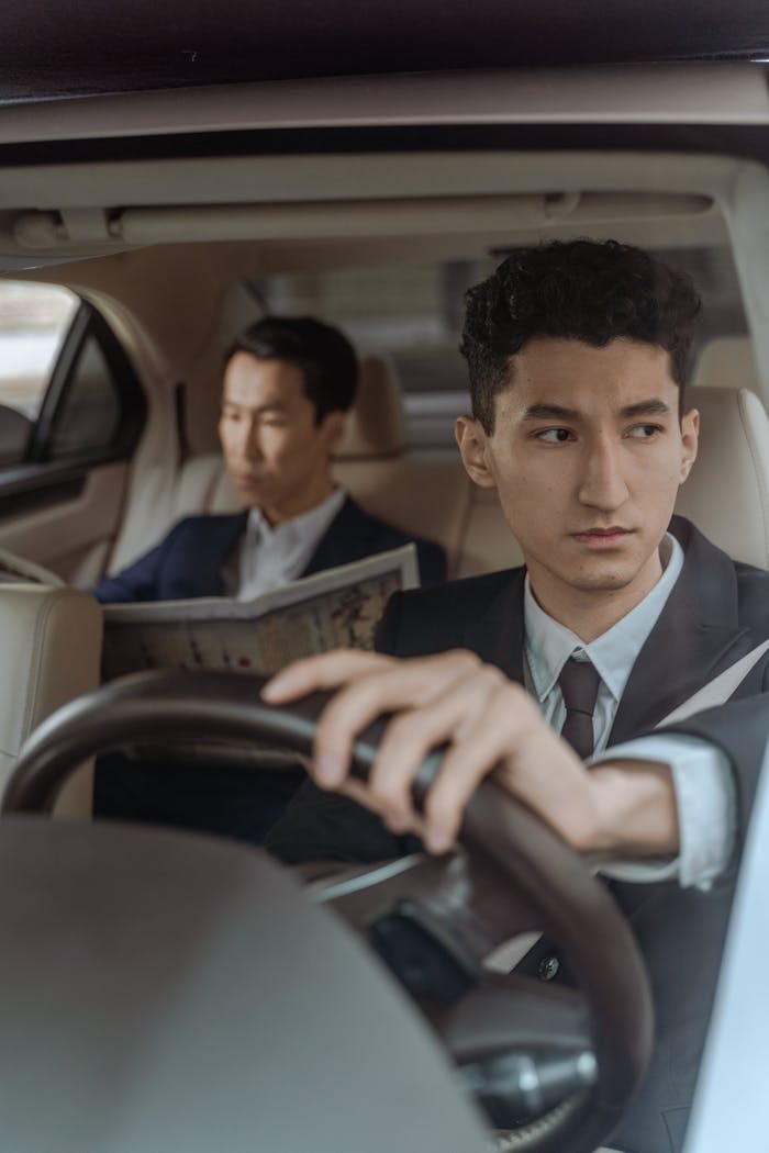 Professional chauffeur driving with attentive passenger reading in a luxury car interior.